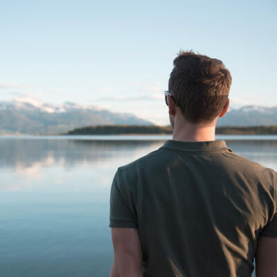 Blick über die Schulter eines Mannes, über einen See hinweg auf die Berge